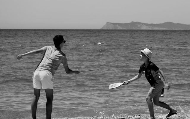 Monochrome image of a man and boy playing paddle ball on a Greek beach.