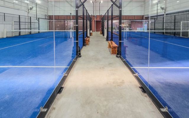 Modern indoor padel tennis courts featuring bright blue surfaces and glass partitions.